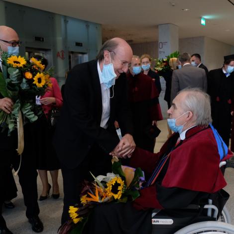 gratulujący profesorowi Zembali mężczyźni z bukietami kwiatów składane 