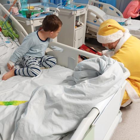 Mały pacjent siedzący na łóżku szpitalnym czekający na prezent od Mikołaja